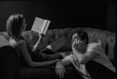 a man and woman sitting on a couch with an open book