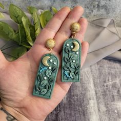 a hand holding two green earrings with stars and moon designs