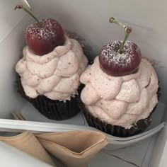 two cupcakes in a box with cherries on top