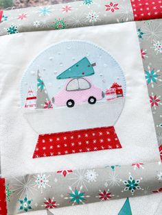 a close up of a patchwork quilt with a snow globe on it and trees in the background