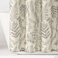 a bath tub sitting next to a shower curtain covered in leaves and flowers on it