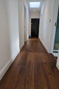 an empty hallway with hard wood flooring and white walls, leading to a black door