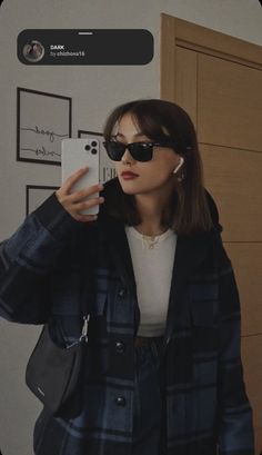 a woman taking a selfie in front of a mirror wearing sunglasses and a coat