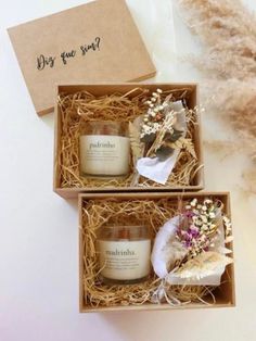 two boxes with candles and flowers in them on a white surface next to some feathers