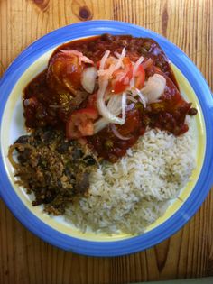 a blue and yellow plate topped with rice and meat covered in tomato sauce next to other food items