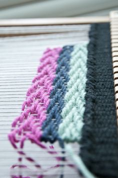 a close up view of a weaving machine with yarn on the side and two different colors