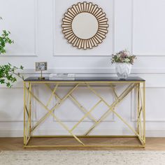 a gold and black console table with a mirror on the wall above it, next to a potted plant