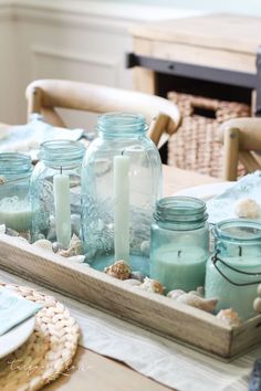 mason jars filled with candles sit on a tray next to shells and seashells