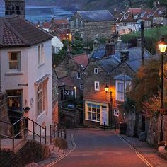 a narrow street with houses on both sides and the ocean in the background at dusk