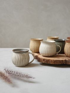 several ceramic cups are sitting on a wooden tray next to a dried plant and a feather