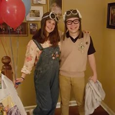 two people standing next to each other in front of balloons and pictures on the wall