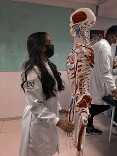 a woman in white lab coat standing next to a skeleton