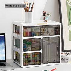 a laptop computer sitting on top of a desk next to a white shelf filled with art supplies