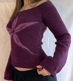 a woman is wearing a purple sweater and black pants with her hands on her hips