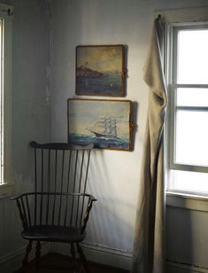 two paintings hang on the wall next to a rocking chair in front of a window