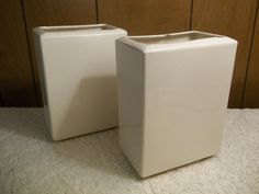 two white square vases sitting on top of a table