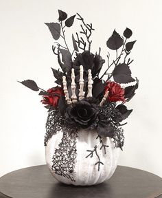 a white pumpkin decorated with black and red flowers on top of a wooden round table