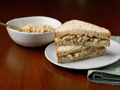 a sandwich cut in half sitting on top of a white plate next to a bowl of salad