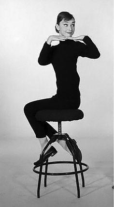 a black and white photo of a woman sitting on a stool posing for the camera