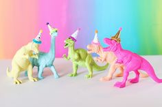 three toy dinosaurs with party hats on and one dinosaur in the process of being photographed