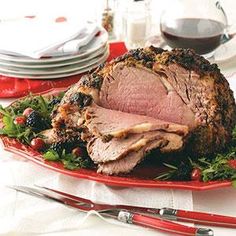 a large roast on a red platter with greens and cranberries next to silverware