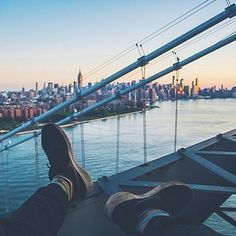 someone is sitting on the edge of a bridge with their feet in the water looking out over a city