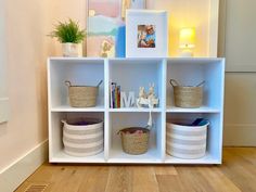 a white shelf with baskets and pictures on it