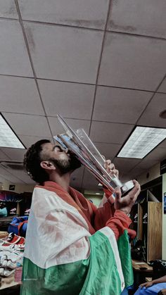 a man in an orange and green shirt is holding up some silver items to his face