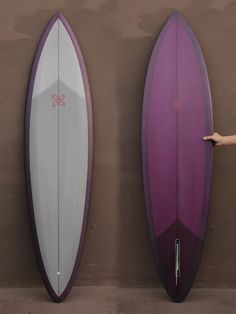 two purple and white surfboards standing next to each other in front of a wall