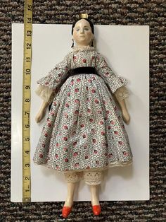 a doll with a measuring tape in front of it on a carpeted floor next to a ruler