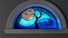 a blue window with a tree and moon in the center, on top of a shelf