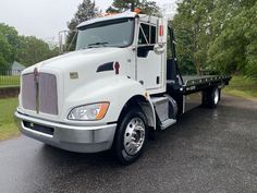 a white semi truck is parked on the side of the road in front of some trees