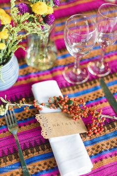 a place setting with flowers, wine glasses and napkins on a colorful table cloth