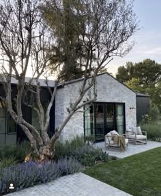 an image of a house that is in the middle of some grass and trees with chairs around it