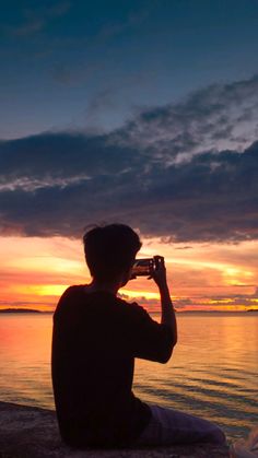 a man sitting on the beach taking a photo at sunset