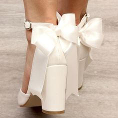 a woman's white high heeled shoes with a large bow