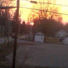 the sun is setting over some houses in an area with no trees or bushes on either side of the road