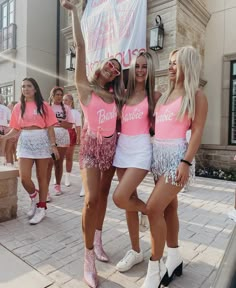 three women in pink and white cheerleader outfits posing for the camera while holding up a sign