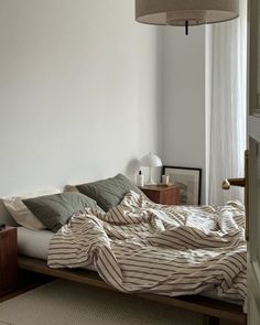 an unmade bed in a bedroom with a lamp hanging above it