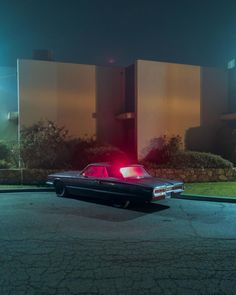 an old car parked in front of a tall building at night with its lights on