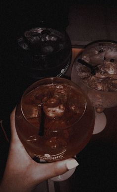 a person holding a drink in their hand with ice on the table next to it