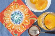 an orange juice in a jar next to two bowls and spoons on a blue table cloth