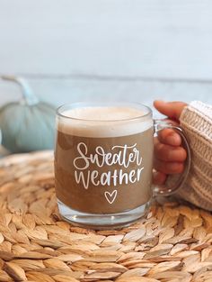 a person holding a coffee mug with the words sweater weather on it, sitting on a wicker table