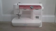 a white sewing machine sitting on top of a carpeted floor next to a wall