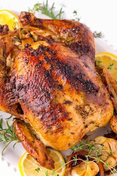 a whole chicken on a plate with lemons and garlic garnished with herbs