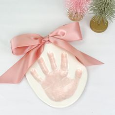 a pink handprint on a white plate with a pink ribbon around it and two small trees in the background