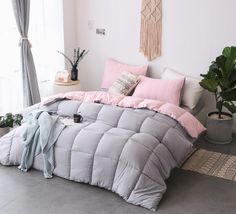 a bed with pink and grey comforters in a room next to a potted plant