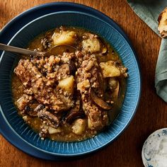 a blue bowl filled with stew next to two slices of bread on a wooden table