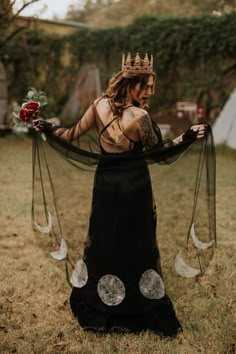 a woman in a black dress with a crown on her head is holding a rose