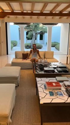 a woman sitting on a couch in a living room with an open floor plan and large windows